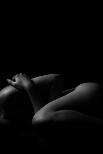 Artistic black and white nude photograph featuring a silhouette of a woman in a studio.
