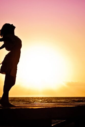 Silhouette of a woman at the beach with arms outstretched against a vibrant sunset backdrop.
