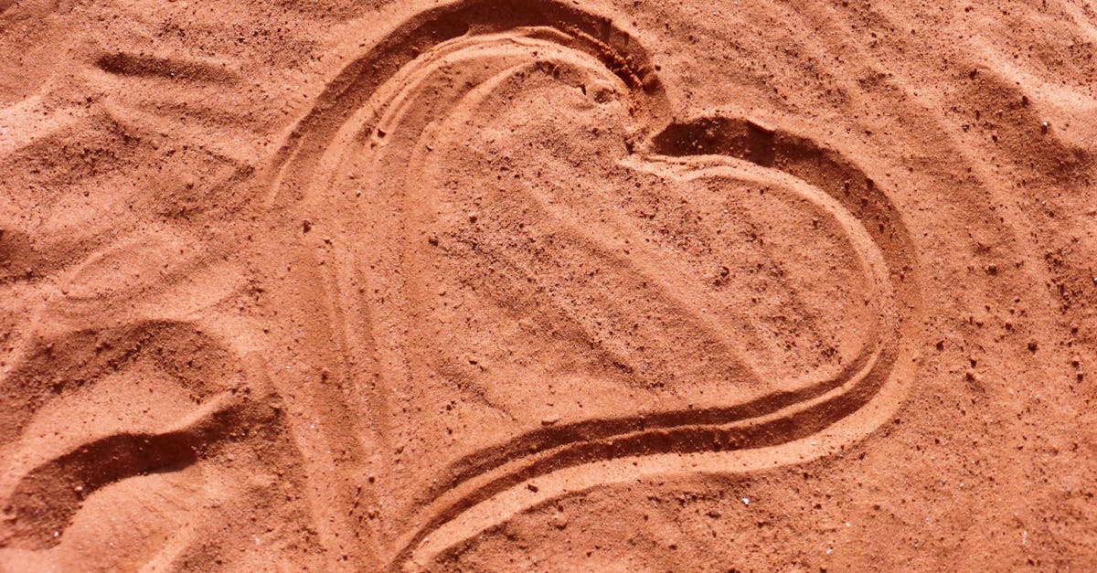Heart shape drawn in soft sand, captured under sunlight, symbolizing love and romance.