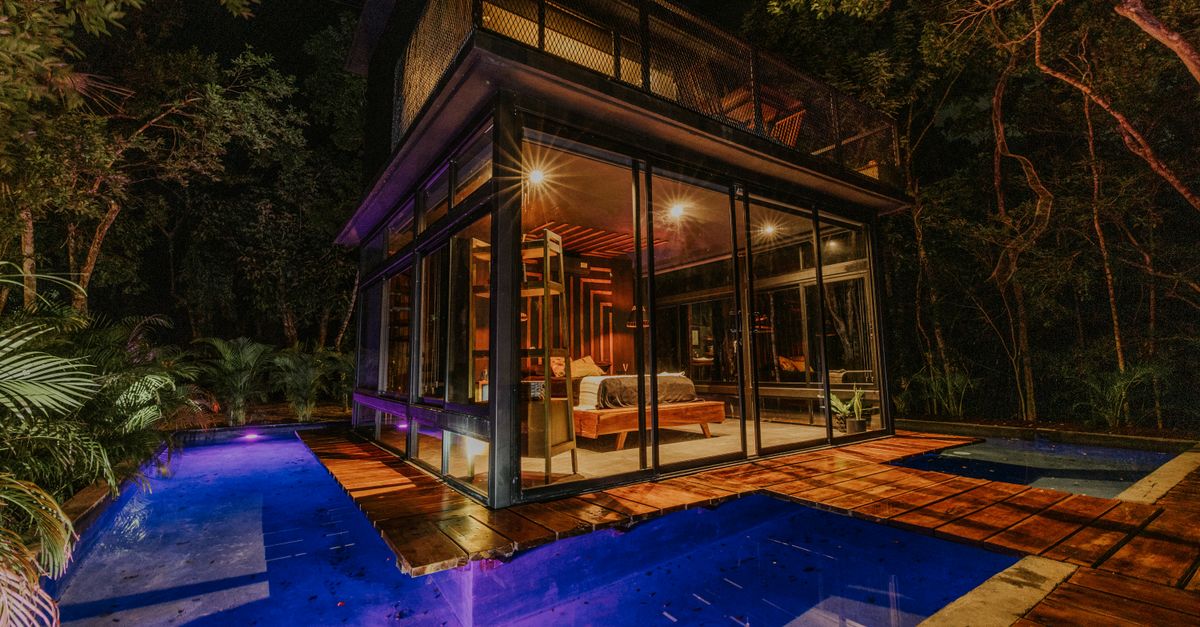 Experience a night in a luxury secluded glass house with a glowing pool surrounded by jungle.