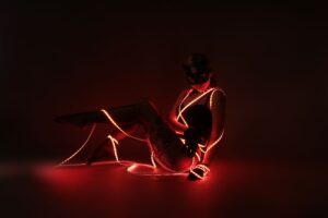Artistic studio shot of a woman wrapped in red LED lights wearing lingerie and a mask.